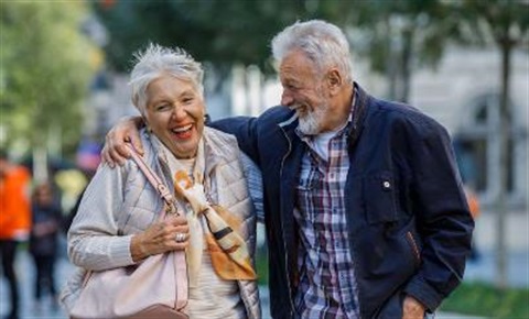 Older couple laughing & walking in park