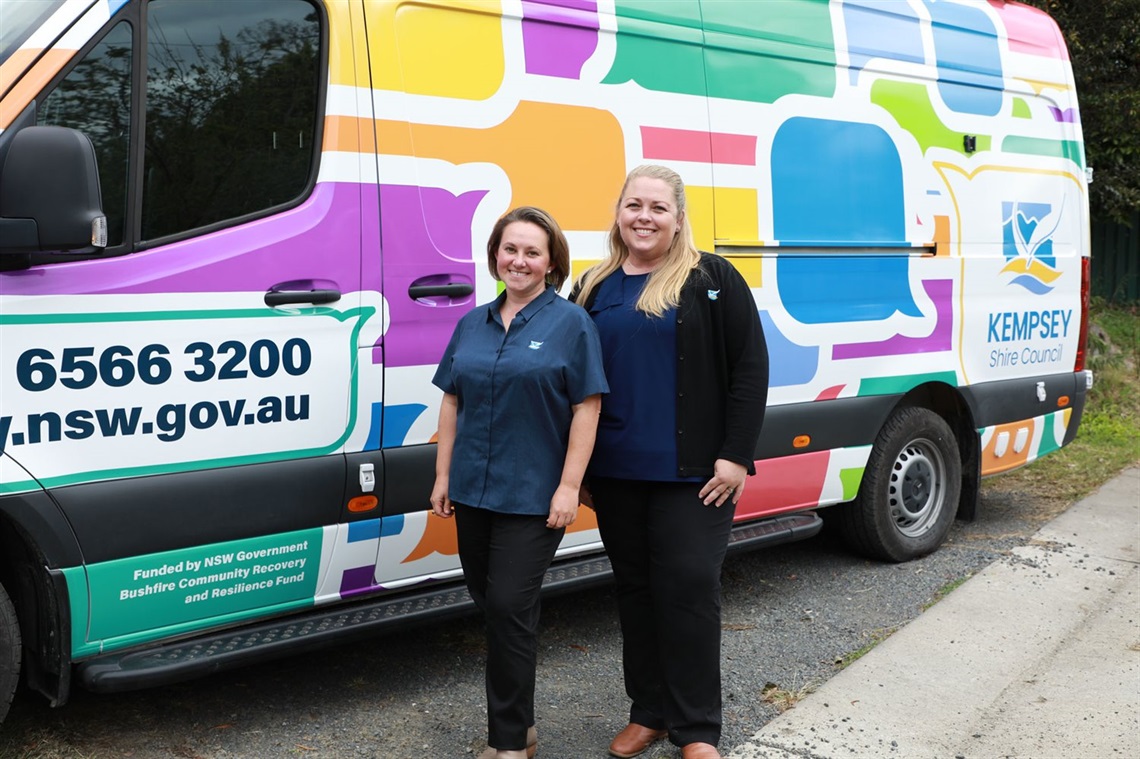 Two ladies standing in front of a corporate vehicle 